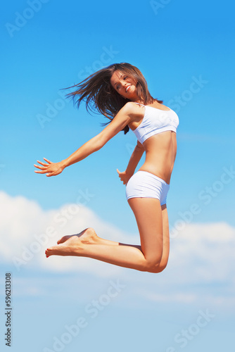 Fototapeta Naklejka Na Ścianę i Meble -  Energy, happy woman and jumping in the air on a blue sky for freedom, summer body and happiness. Smile, excited jump and a girl in underwear for comfort, free and positivity with a boost in vitality
