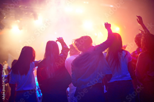 Crowd, people dancing at concert or music festival from back, neon lights and energy at live event. Dance, fun and group of excited fans in arena at rock band performance or audience at rave party.