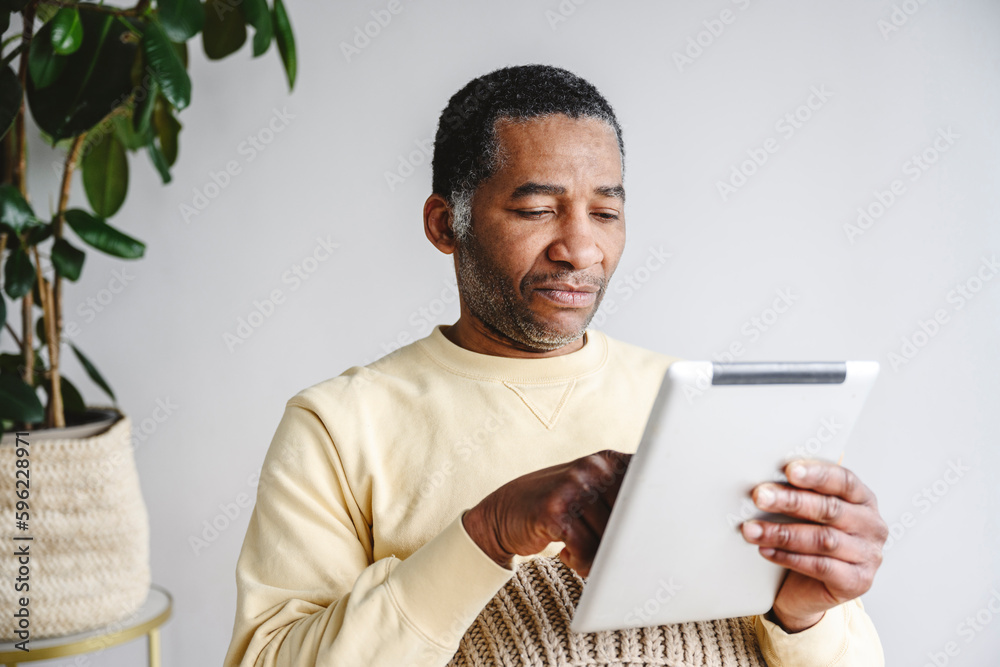 Man using tablet PC sitting in front of wall at home Man using tablet PC sitting in front of wall at home
