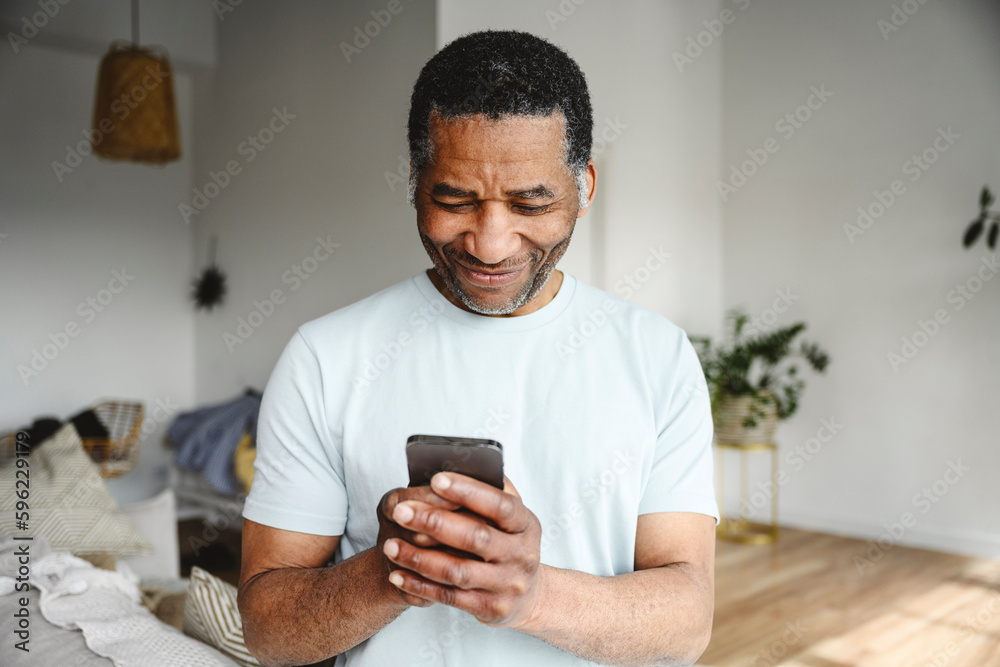 Smiling mature man using mobile phone in living room at home Smiling mature man using mobile phone in living room at home