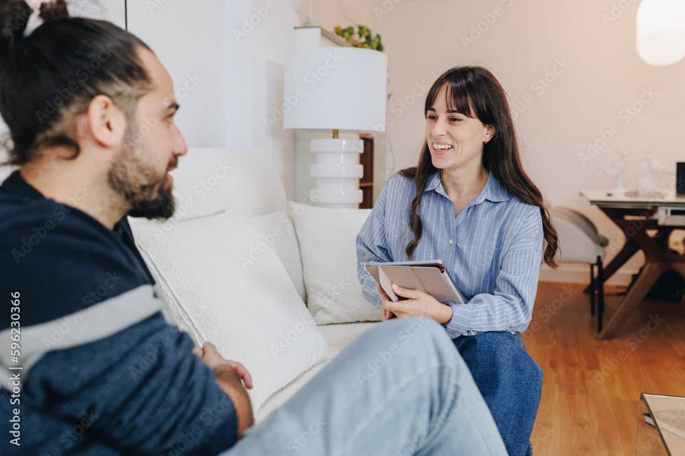 Smiling nutritionist with tablet PC advising client sitting on sofa at home Smiling nutritionist with tablet PC advising client sitting on sofa at home
