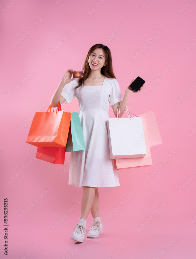 full body image of asian woman holding shopping bag and posing on pink background