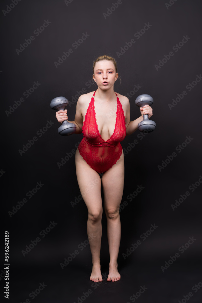 Beautiful model in sportswear with dumbbells looks at the camera on yellow, red and dark background
