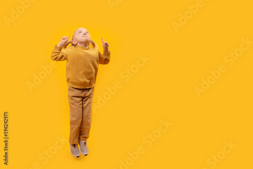 Child looks up and points her fingers up. Studio portrait of girl in yellow suit on bright yellow background. Copy space, mock up