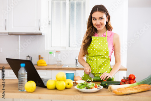 Woman cook reads the recipe in laptop and cooks salad in kitchen