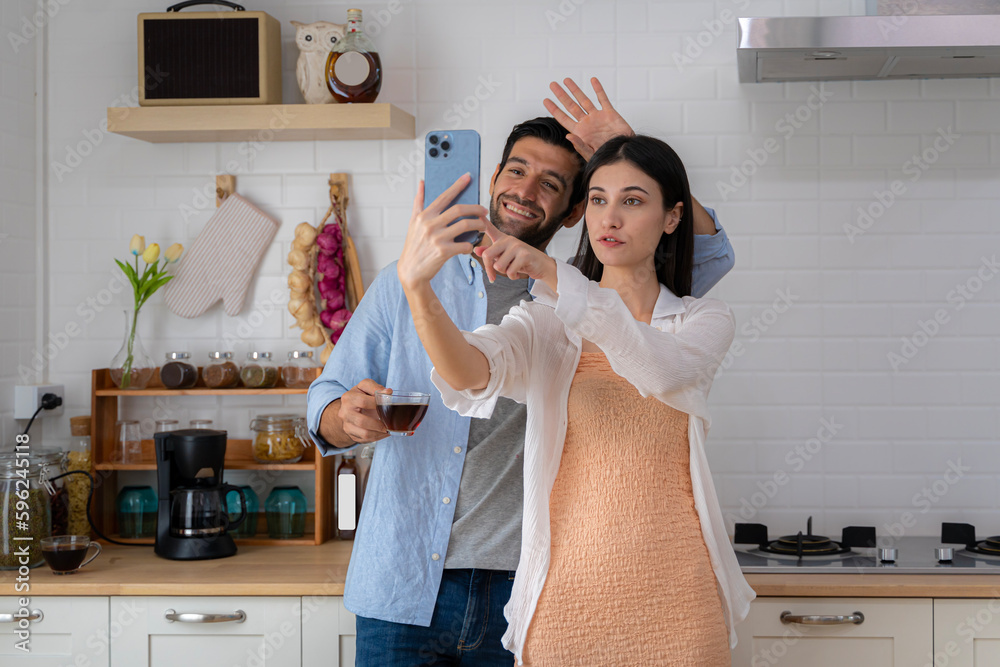 Young couple hugging and smiling at the camera Standing in the kitchen drinking morning coffee, using social media to communicate with friends and family, taking selfie Young couple hugging and smiling at the camera Standing in the kitchen drinking morning coffee, using social media to communicate with friends and family, taking selfie