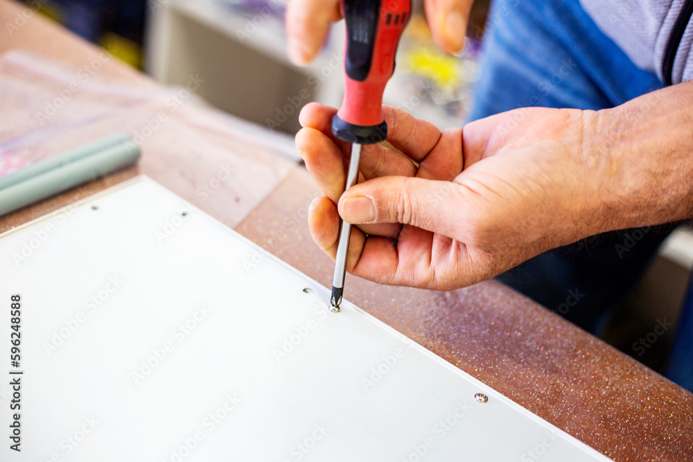Close up of a man's hands using a screwdriver to assemble a furniture with copy space, selective focus