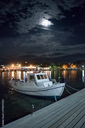 Porto Rafti town. Night illumination, reflections of buildings and small fishing boat in the  marina. Greece.