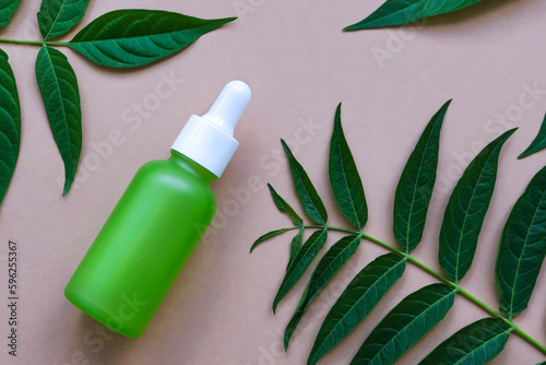 Green glass dropper bottle with natural green leaves on a beige background. Natural, organic cosmetics.