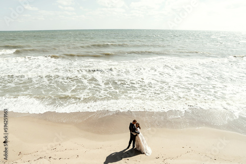Drone photo of the newlyweds walking along the beautiful beach. Scenic aerial view of a happy romantic couple waking up together by the ocean. beach wedding