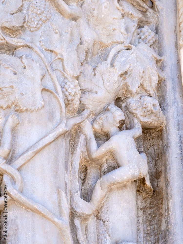 Marble details on facade of Messina Cathedral or Duomo di Messina, Sicily, Italy. Reliefs on wall picturing human figures harvesting grapes. Decorative elements in architecture