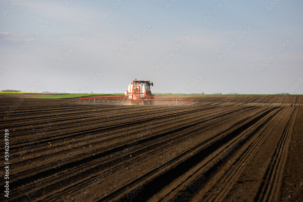 Fototapeta premium Tractor spraying land in sunset.