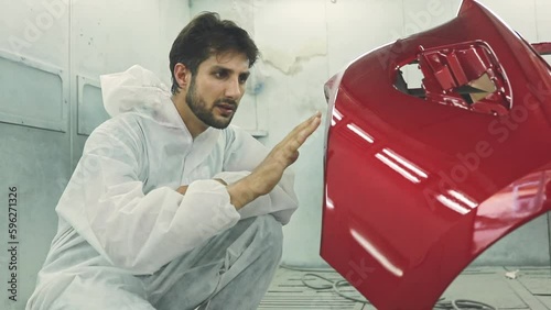 Skilled painter White uniform sits admiring the masterpiece painted red fiberglass front bumper of a restored car giving thumbs up in the paint room.