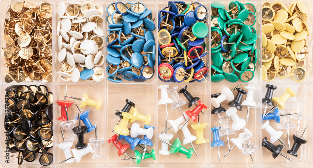 Fototapeta premium Plastic box with different multi-colored pushpins on wooden background