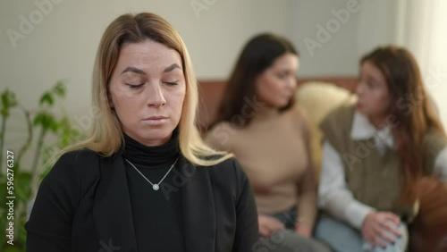 Portrait of calm confident therapist listening to teen girl arguing with young woman at background standing up leaving. Professional Caucasian female psychologist with irritated patients indoors photo