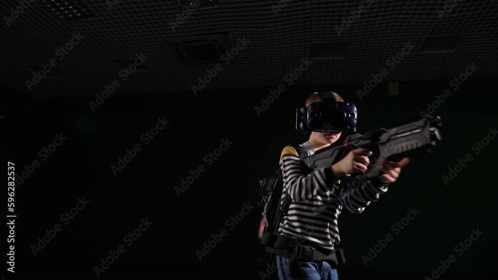 A teenage child using a VR headset helmet and an automatic controller to simulate a game on a black background. The child passes obstacles in the virtual world in the game studio. A teenage child using a VR headset helmet and an automatic controller to simulate a game on a black background. The child passes obstacles in the virtual world in the game studio.
