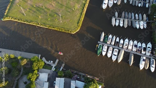 An orbiting aerial shot of a sail boat arriving at the yacht club in Náutico San Isidro, Buenos Aires. The setting is during the sunset. photo