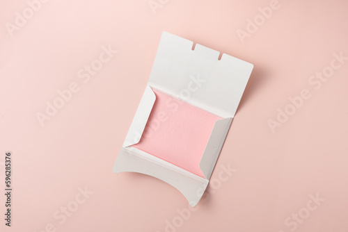 White package with pink facial oil blotting tissues on light pink background. Shine control, skin care mattifying wipes