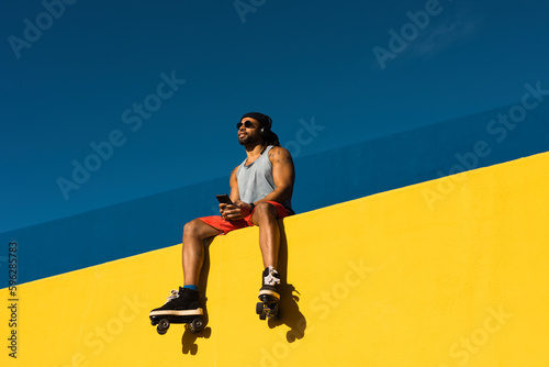 Black man listening music outside. Urban man posing with roller skates.