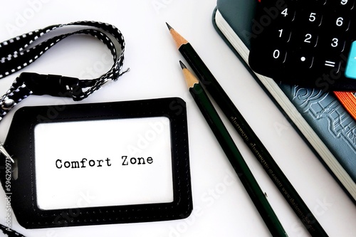 Desk office equipments (pencils/notebook/calculator) and ID staff card with text written COMFORT ZONE, concept of living the same old lifestyle for safety