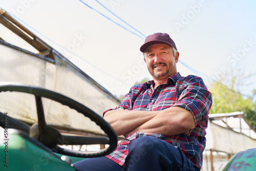Smiling male farmer sitting with arms crossed on tractor