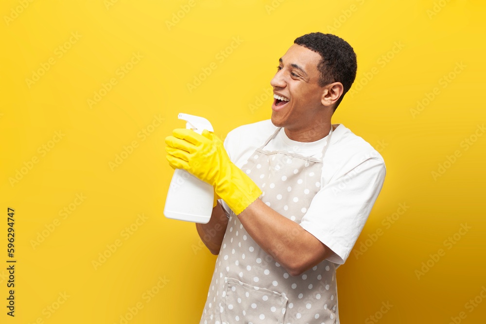 guy african american cleaner in apron holds gloves and detergent on yellow isolated background, cleaning service guy african american cleaner in apron holds gloves and detergent on yellow isolated background, cleaning service