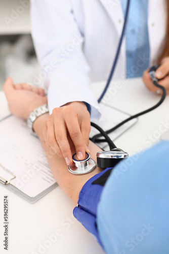 Cardiologist doctor measures blood pressure to patient with tonometer in clinic. Diagnosis of arterial hypertension and problems with pressure