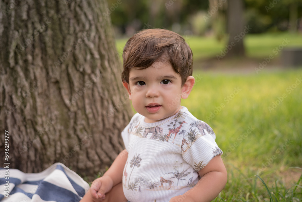 Little boy looking at the camera while sitting outdoors in a park. Little boy looking at the camera while sitting outdoors in a park.