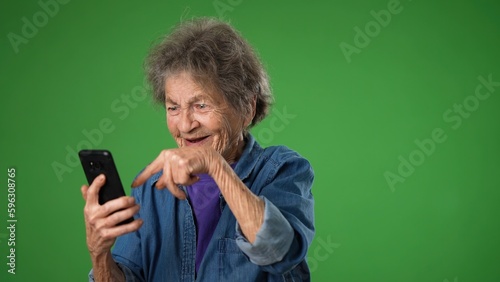 Funny crazy elderly old toothless woman answering smart phone call say wow as winner with success pointing. Isolated on green screen background.