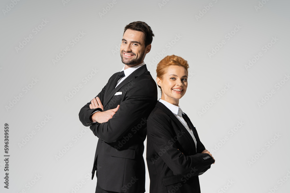 successful corporate managers in black suits standing back to back and smiling at camera isolated on grey. successful corporate managers in black suits standing back to back and smiling at camera isolated on grey.