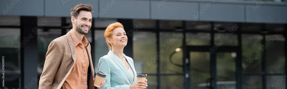 happy business partners with takeaway drinks looking away and smiling on urban street, banner. happy business partners with takeaway drinks looking away and smiling on urban street, banner.