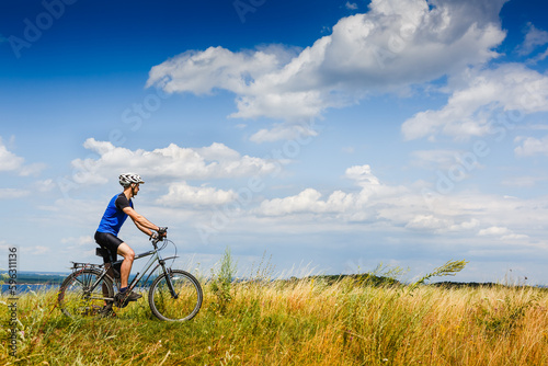 young athletic man on a bicycle riding the green meadow trail on sunny day