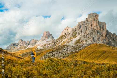Tourist in yellow jacket and backpack enjoying the exploration amidst the towering mountains of the famous Giau Pass.  © vladim_ka