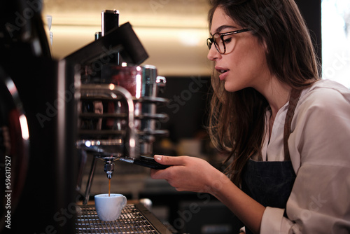 Barista standing in a coffee shop and making espresso on a coffee machine.