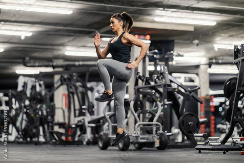 A sportswoman is jumping in place in a gym and doing cardio exercises.