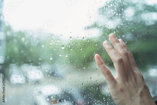 Close up of hand on a rain soaked window with blurry outside view background. photo