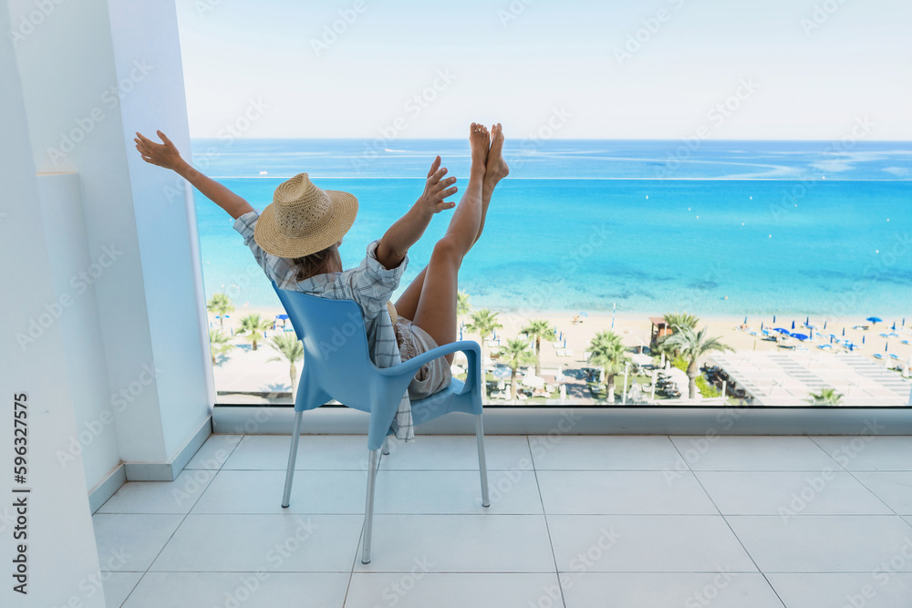 Young woman relaxing in chair on balcony of beachfront hotel or apartment Young woman relaxing in chair on balcony of beachfront hotel or apartment