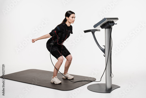 Foto Fitness girl in EMS suit is doing workout sport training that uses electrical impulses to stimulate muscles on white background