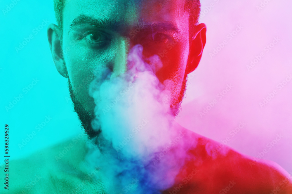 Fototapeta premium Handsome young man with wet skin in colorful light smoking cigarette or marijuana