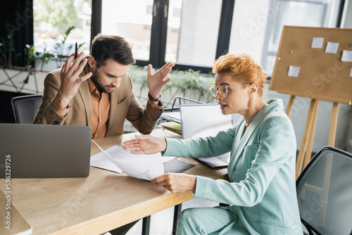 Tablou pe pânză displeased businesswoman pointing at document while talking to shocked manager in office