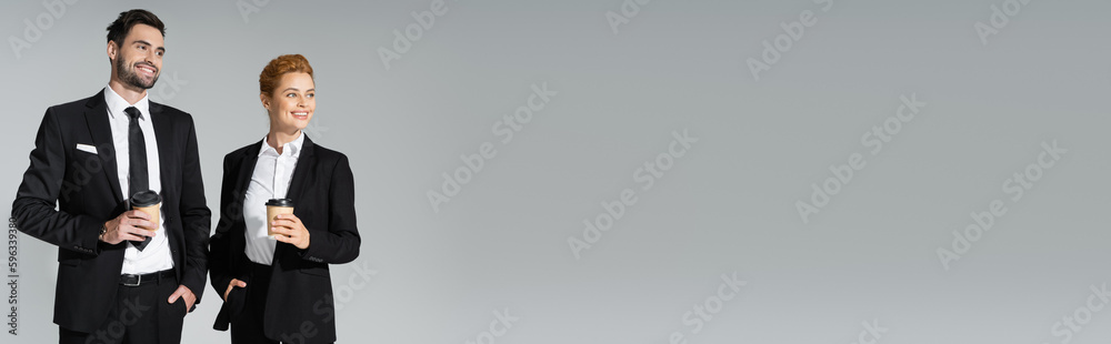 happy business partners holding paper cups and looking away isolated on grey, banner. happy business partners holding paper cups and looking away isolated on grey, banner.