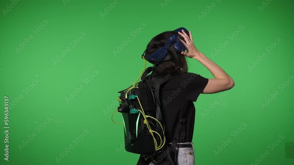 Portrait of a young woman in a virtual reality headset in a studio on a green background, she looks around emotionally in the virtual world. Chromakey. 3D glasses.
