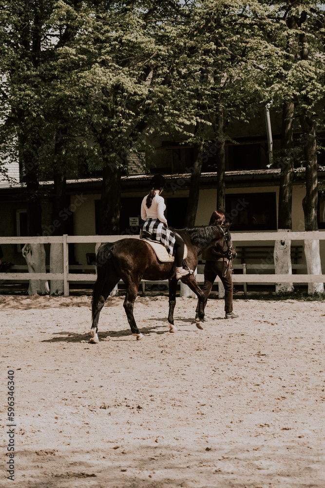 A woman instructor teaching girl how to ride a horse. Female rider practicing on a horseback learning equestrian sport. Active lifestyle and leisure activity concep A woman instructor teaching girl how to ride a horse. Female rider practicing on a horseback learning equestrian sport. Active lifestyle and leisure activity concep