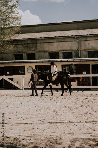 A woman instructor teaching girl how to ride a horse. Female rider practicing on a horseback learning equestrian sport. Active lifestyle and leisure activity concep