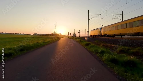 Riding on a cycling way during morning sunrise with train passing on a near railway