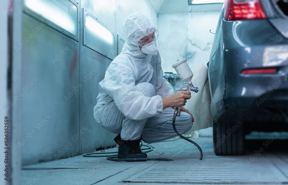 Mechanic painting car in chamber. Worker using spray gun and airbrush