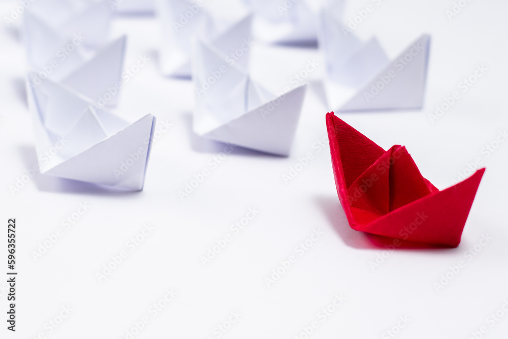 High angle close up shot of a red paper boat followed by many white boats. High angle close up shot of a red paper boat followed by many white boats.