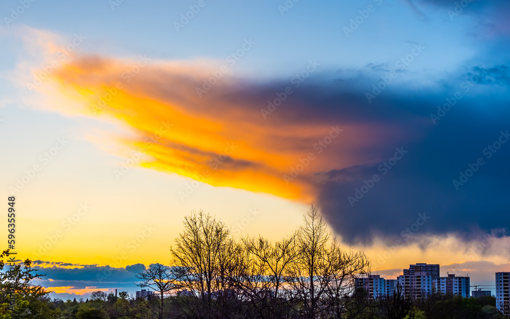 Sunlit colored rain cloud over city at sunset
