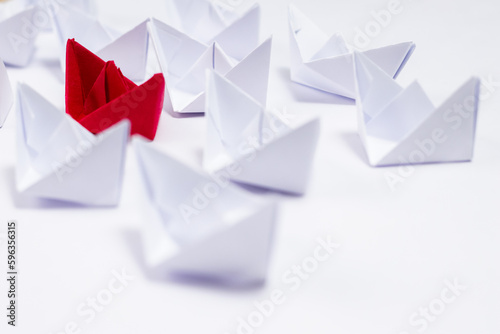High angle shot of white paper boats defocused with one red boat in the middle.