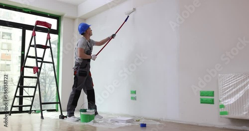 House painter paints wall white with roller. Painting walls or ceiling in apartment